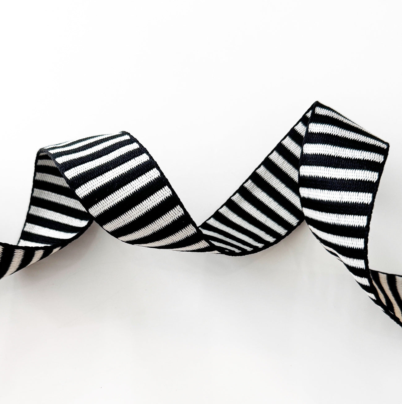 A clean studio shot of wavy, textured black and white striped jacquard woven webbing strap on a solid white background