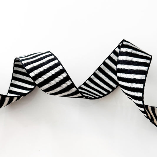 A clean studio shot of wavy, textured black and white striped jacquard woven webbing strap on a solid white background