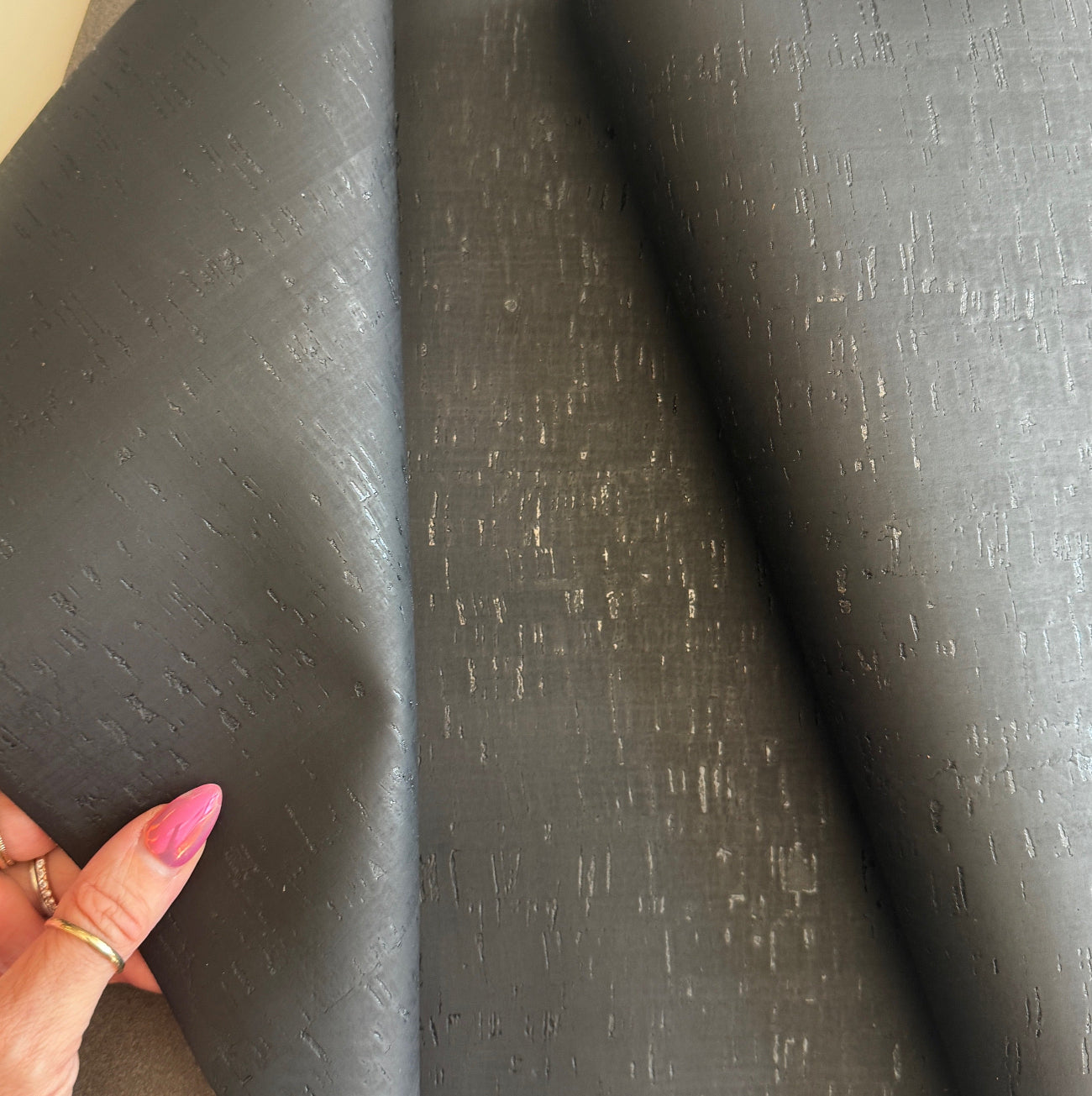 Black cork textured fabric with a hand holding it