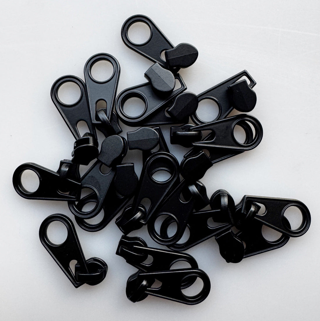 A pile of small black zipper pull tabs or zipper teeth components on a plain white background.