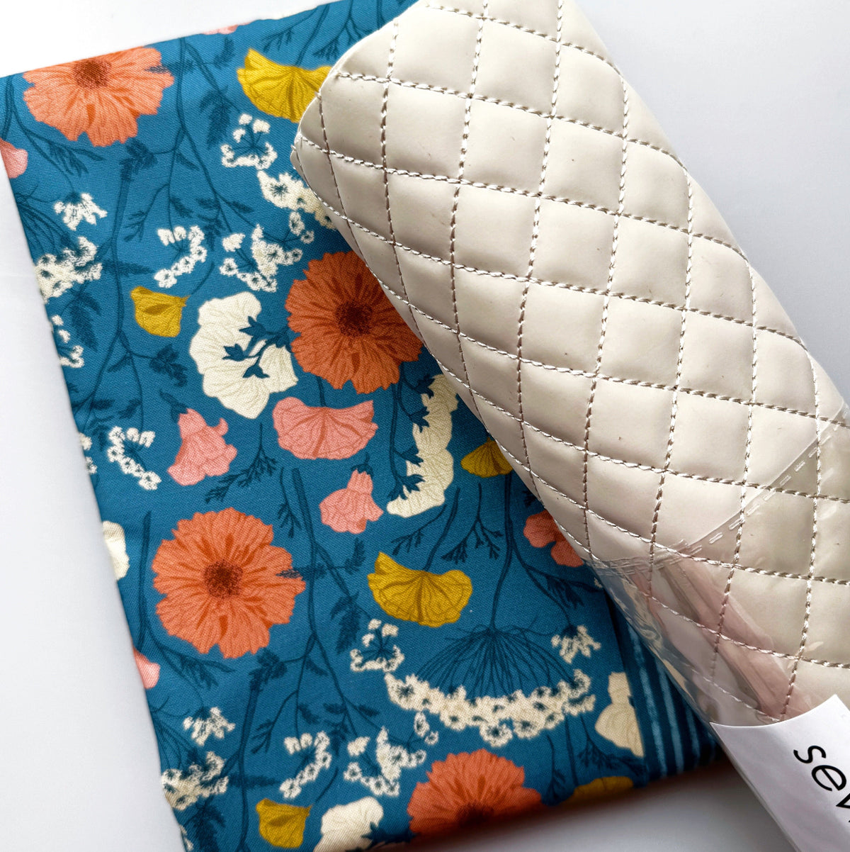 Blue floral fabric with colorful flowers and white quilted vinyl for sewing and bag making.