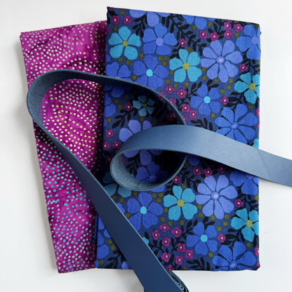 Two folded craft fabrics featuring a blue floral retro print and a magenta dotted pattern, overlaid with a blue leather strap for a DIY project.