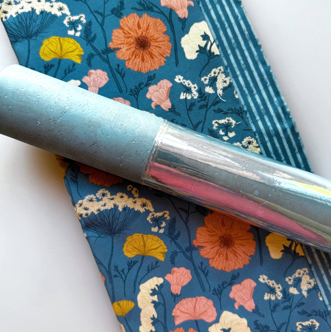 Blue floral fabric featuring colorful flowers and a coordinating light blue sewing tool.