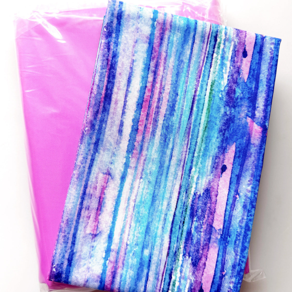 Blue and pink watercolor-style fabric paired with a bright pink bonded nylon pack for sewing and bag making.