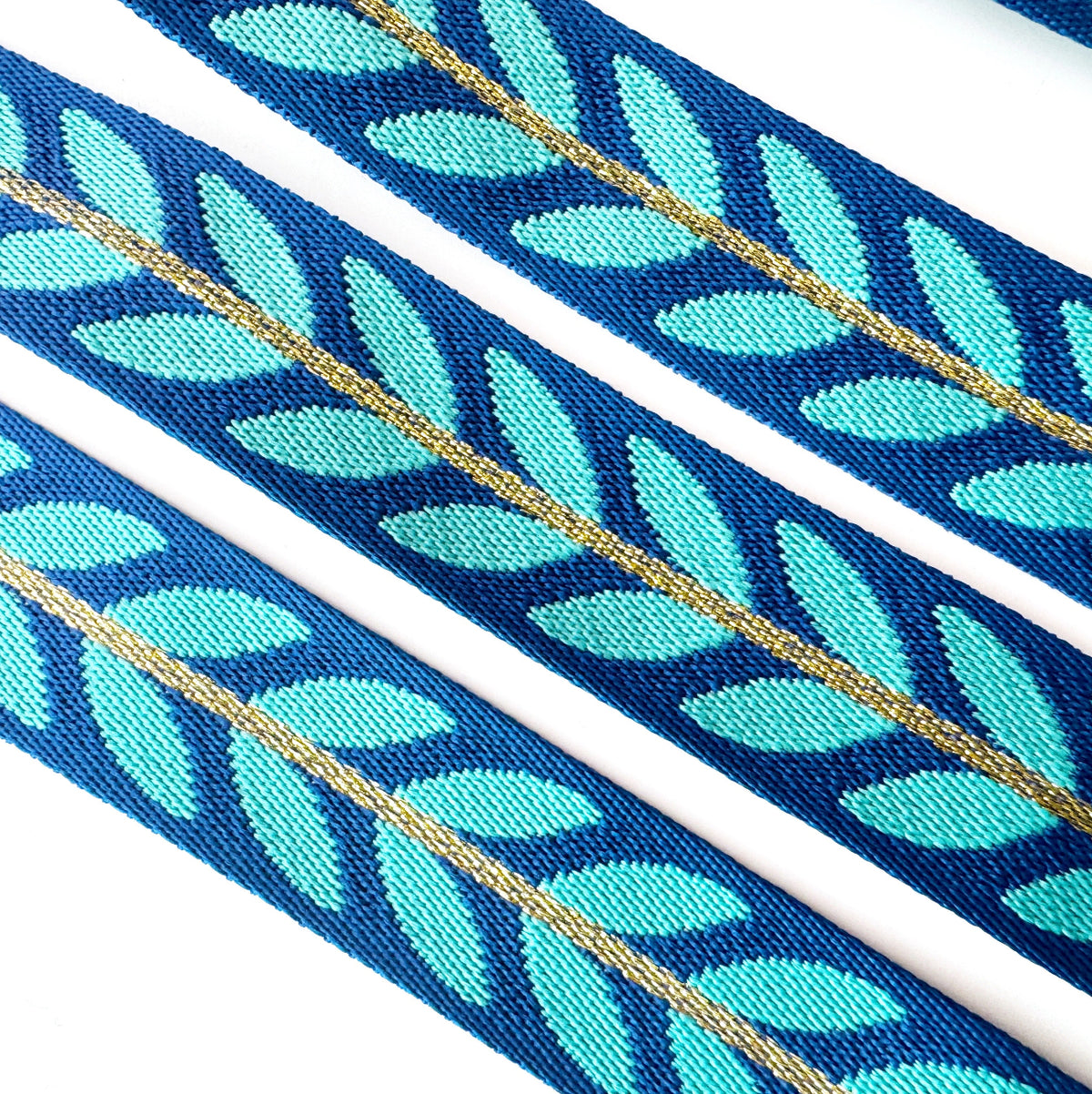 A blue and turquoise leaf-patterned jacquard ribbon trim with a central gold accent line for bag strap and webbing