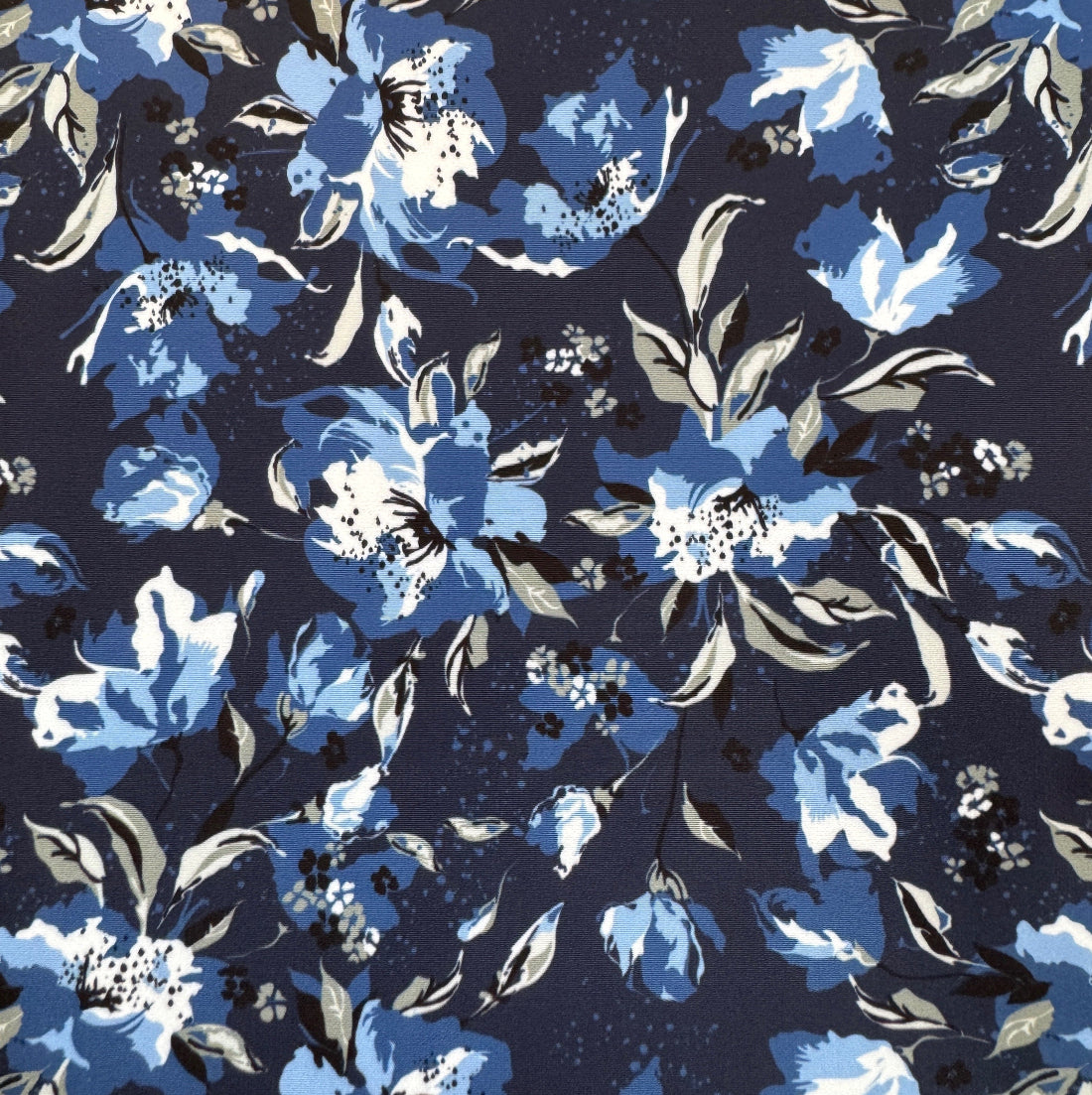 A close-up of a floral fabric pattern featuring blue, light blue, and white flowers with gray leaves on a dark navy background.