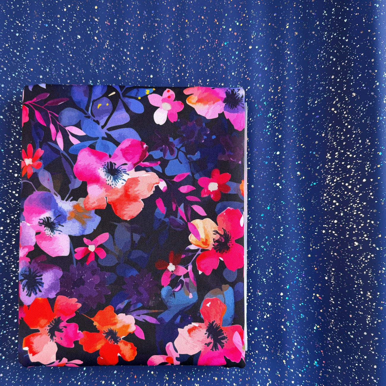 A pack of bonded nylon fabric with a vibrant pink, orange, and purple floral pattern on a dark background, set against a shimmering royal blue glitter vinyl sheet.