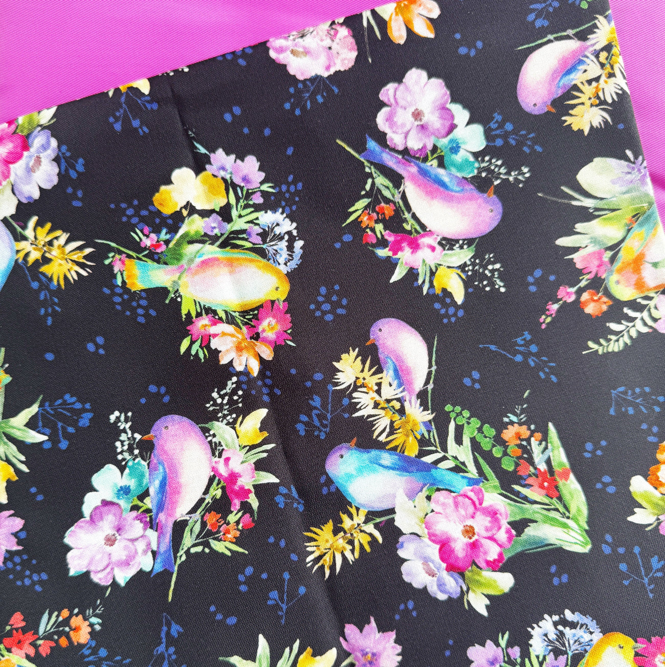 Close-up product photo of a black cotton fabric yard with a colorful bird and floral print layered over bright pink bonded nylon.