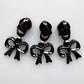 Three glossy black bow-shaped jewelry charms with matching backings, arranged side by side on a plain white background.