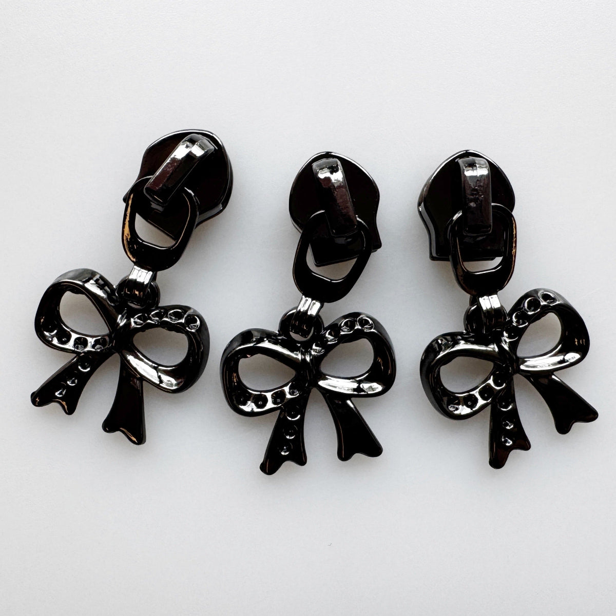 Three glossy black bow-shaped jewelry charms with matching backings, arranged side by side on a plain white background.