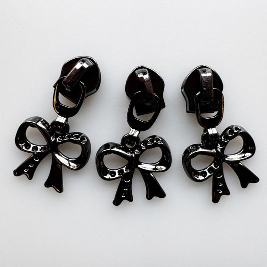 Three glossy black bow-shaped jewelry charms with matching backings, arranged side by side on a plain white background.