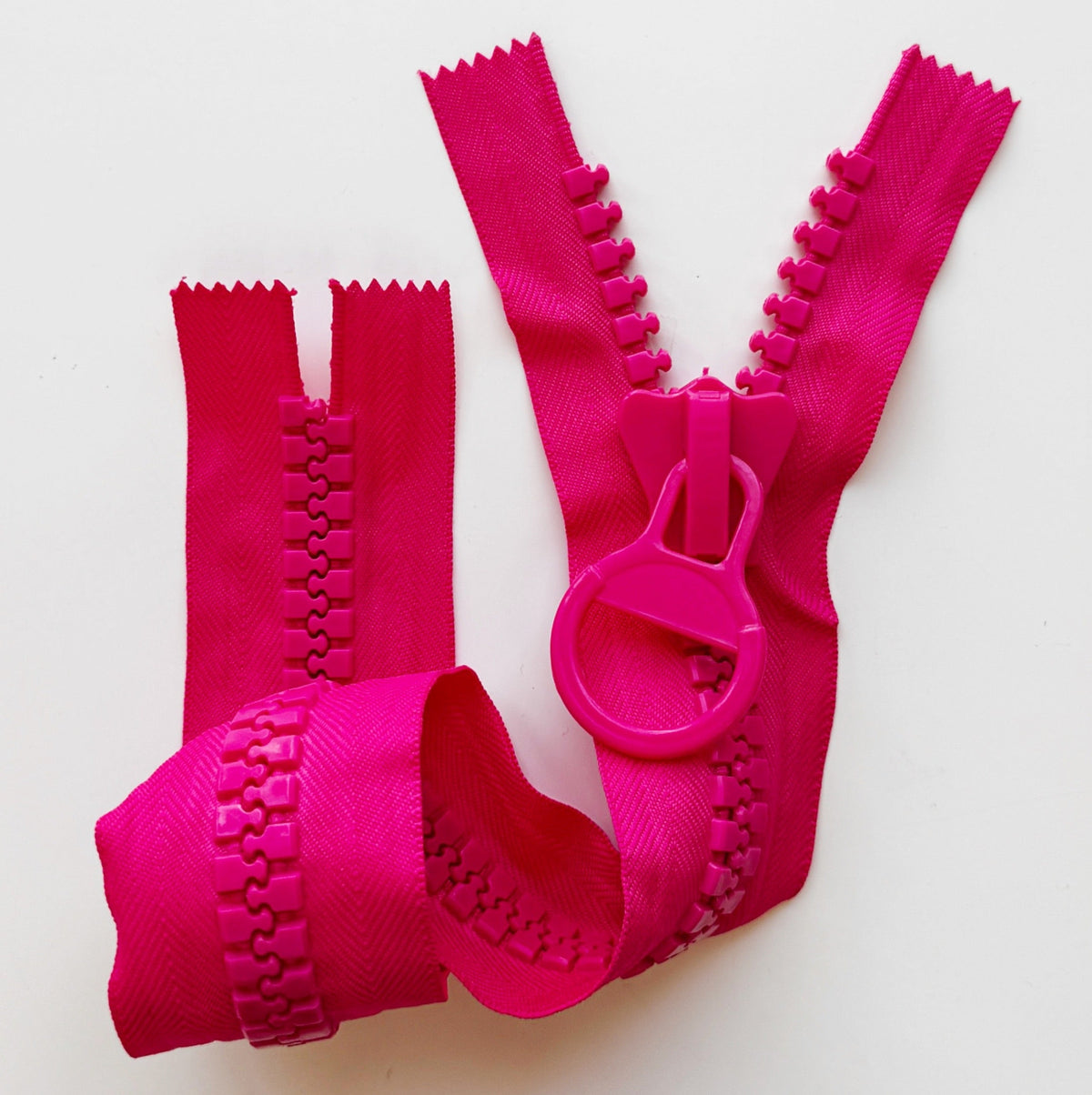 Chunky bright pink molded plastic zipper with large interlocking teeth, matching circular ring pull, and wide fabric tape