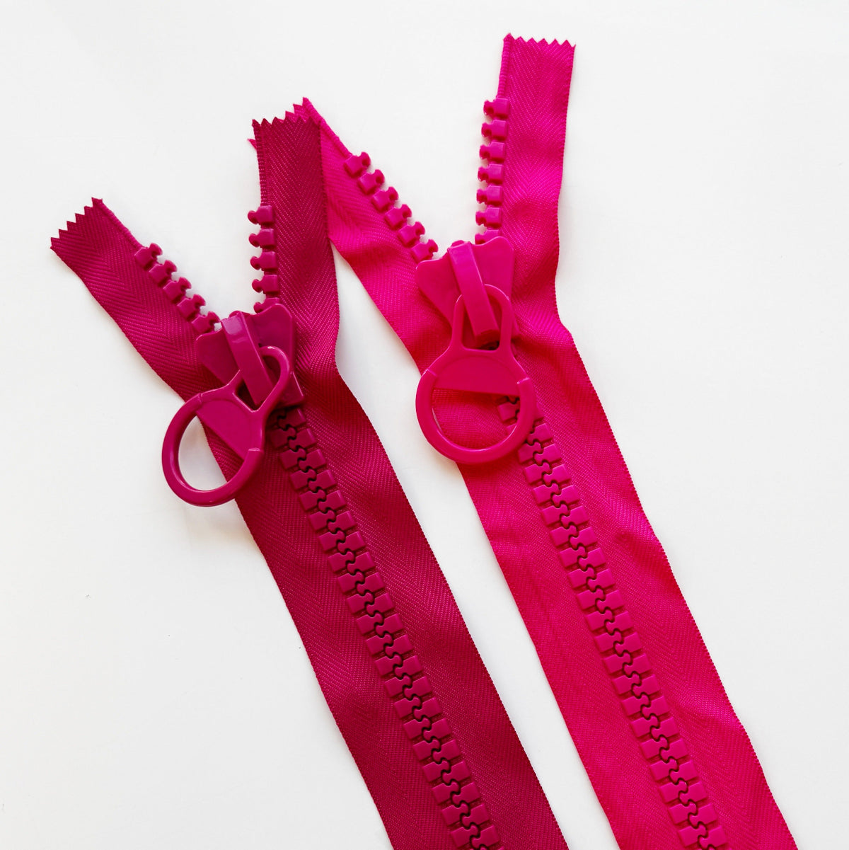 Color comparison of chunky zippers with circular ring pulls in bright pink on top and raspberry on the bottom