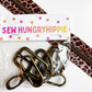 A clear plastic bag containing several bronze-toned metal zipper pulls, sealed with a white paper header card printed with the brand name 'SEW HUNGRYHIPPIE' and small colorful flower motifs. A leopard-print zipper tape strip runs diagonally across the top right on a white background.