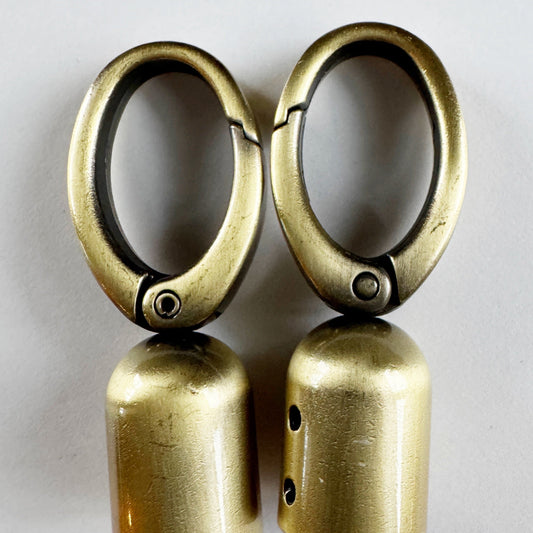 Pair of brass tassel caps  on a reflective surface with a light gray background