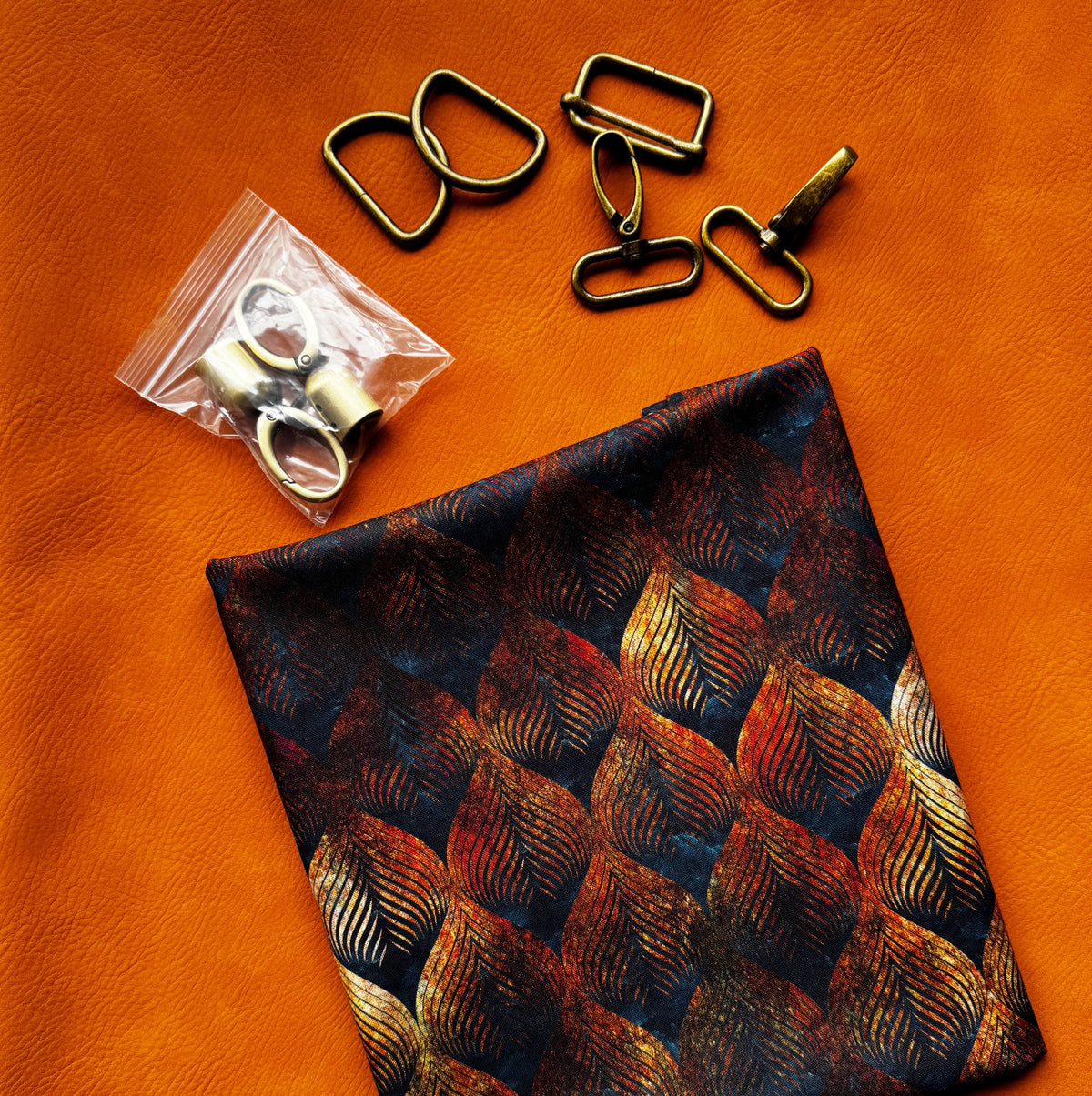 Brown textured faux leather with dark leaf print fabric and gold-tone bag hardware arranged for a sewing project.