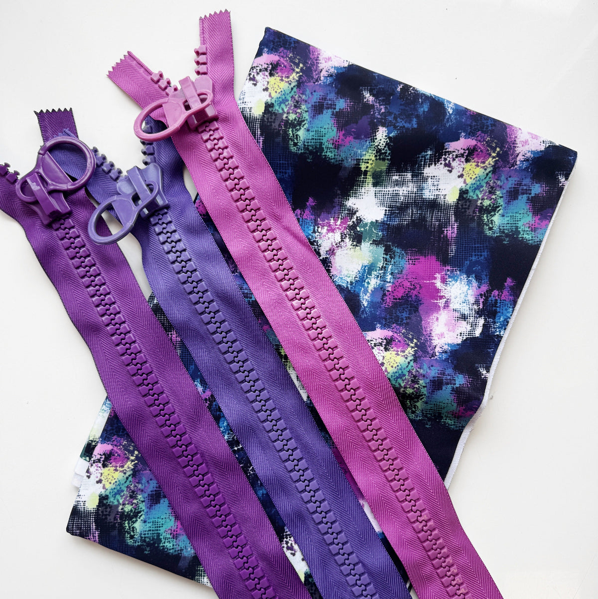Folded Brushstroke Bonded Nylon fabric for bag making paired with chunky zippers in purple, grape purple, and gumdrop