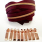 A coiled burgundy zipper ribbon with a metallic rose gold zipper running along the top, displayed above a row of matching rose gold zipper pull tabs on a white background.
