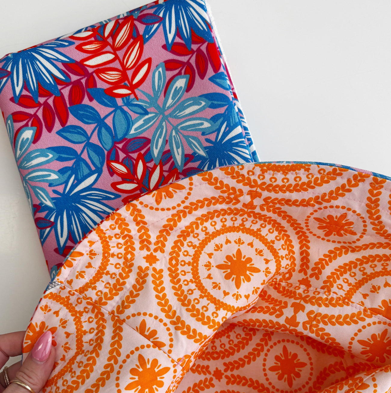 A hand holding a sewn bag lining made from the orange floral medallion fabric, showing how beautifully it coordinates with the pink and blue tropical leaf print canvas from the Canvas Club subscription.