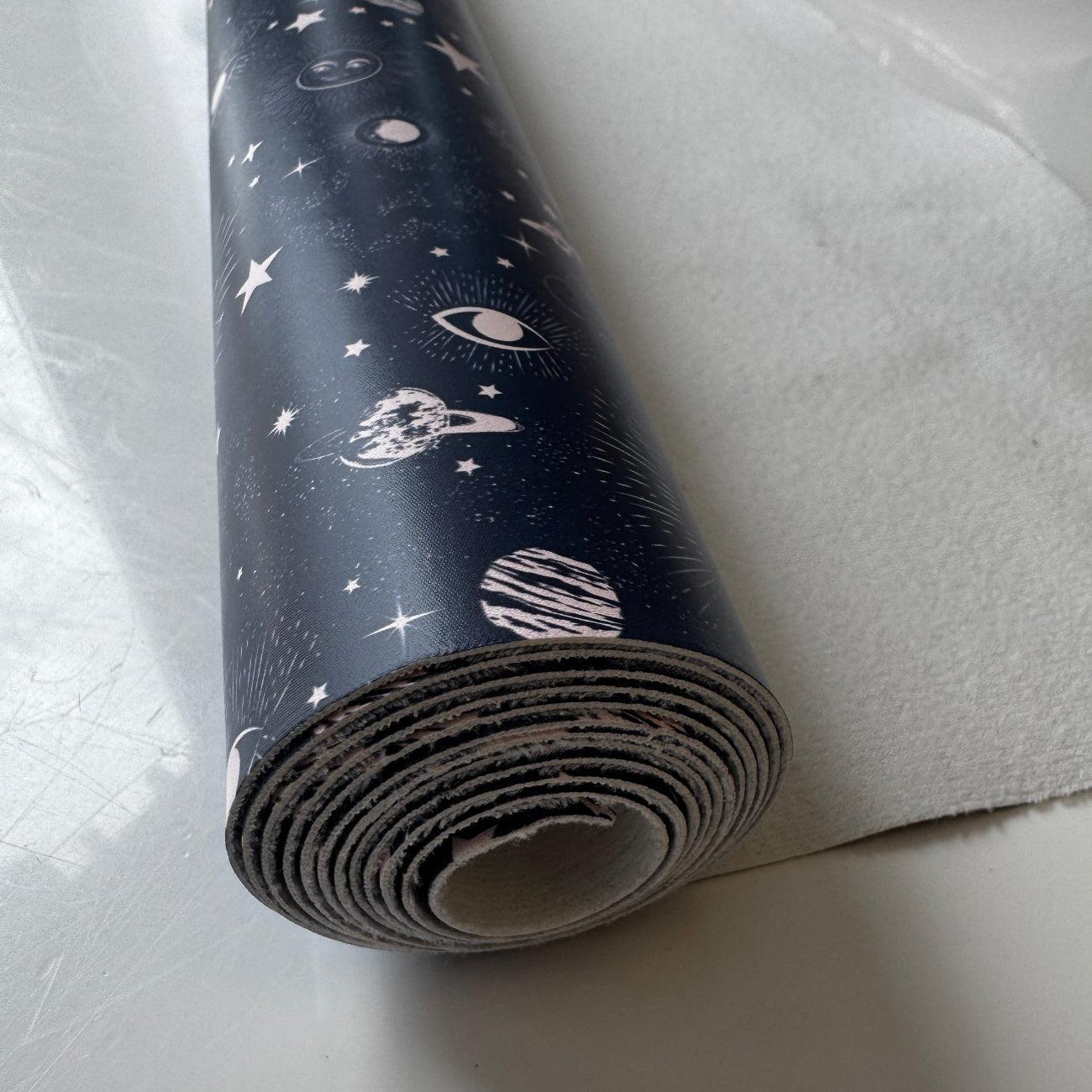 Roll of space-themed vinyl fabric on a light gray surface