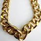 Close-up detail of a thick, chunky gold tone acrylic bag chain with shiny, large links on a clean white background