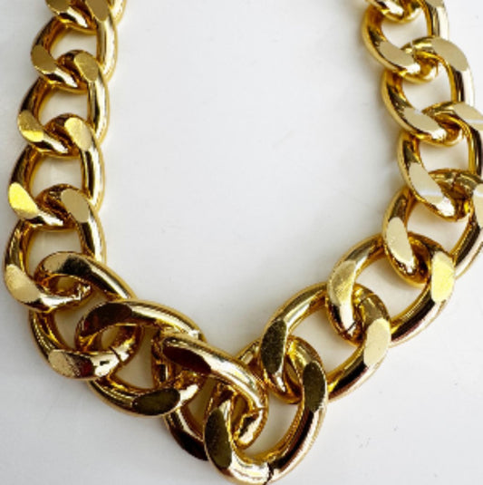 Close-up detail of a thick, chunky gold tone acrylic bag chain with shiny, large links on a clean white background