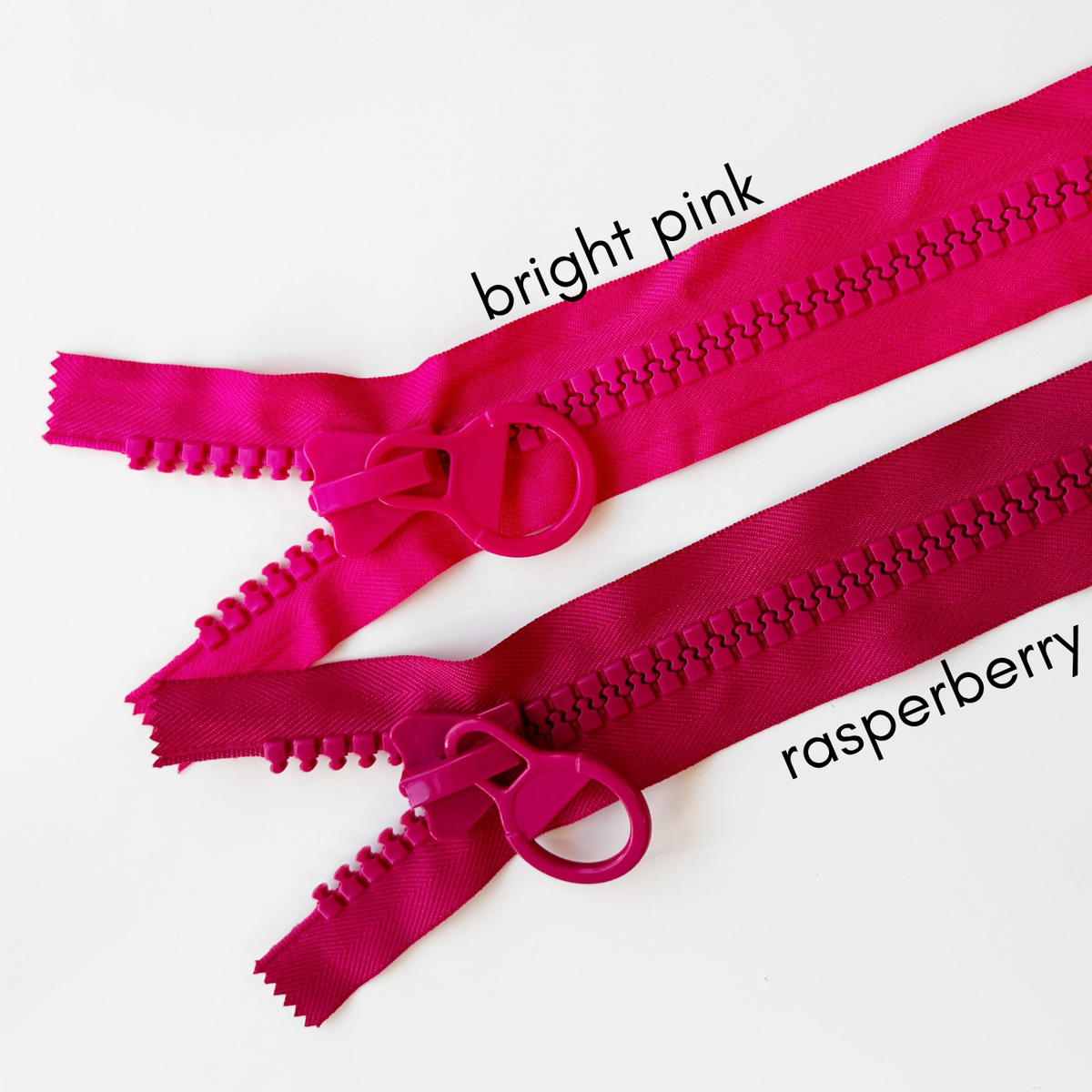 Comparison of chunky resin zippers with oversized circular ring pulls in raspberry and bright pink, featuring large plastic teeth on a white background