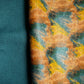 A folded piece of fabric with an abstract brushstroke pattern in mustard yellow, teal, and brown, with a solid teal folded section showing the reverse side, displayed on a white background.
