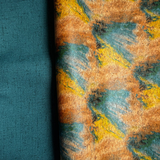 A folded piece of fabric with an abstract brushstroke pattern in mustard yellow, teal, and brown, with a solid teal folded section showing the reverse side, displayed on a white background.