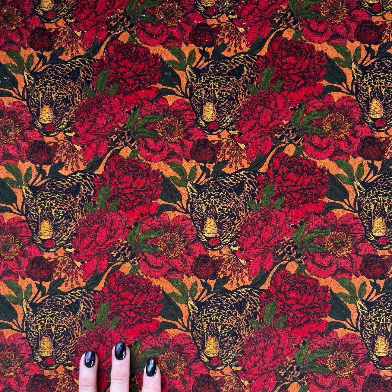 Fabric with red floral and deer pattern held by a hand