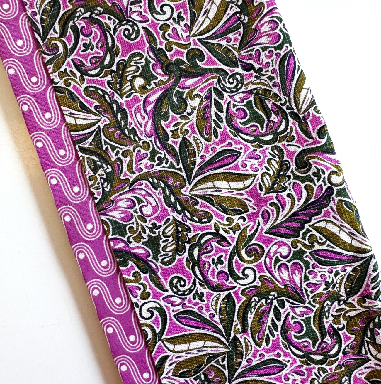 Two folded cotton fabric features a vibrant magenta and green botanical pattern on a white background