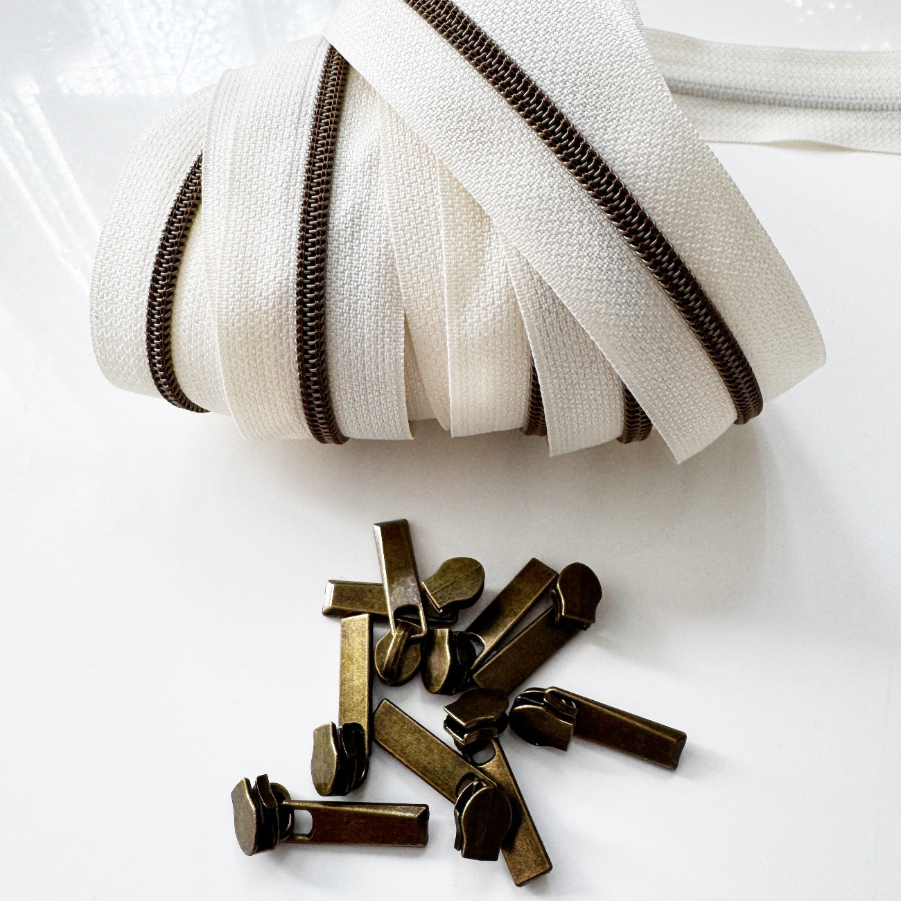Cream #5 continuous zipper tape with antique brass zipper teeth and coordinating antique brass zipper pulls for handbags, wallets, backpacks, pouches, and sewing projects.