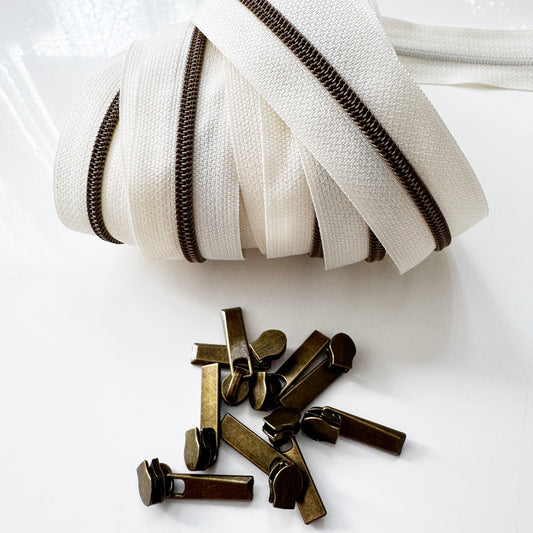 Cream #5 continuous zipper tape with antique brass zipper teeth and coordinating antique brass zipper pulls for handbags, wallets, backpacks, pouches, and sewing projects.