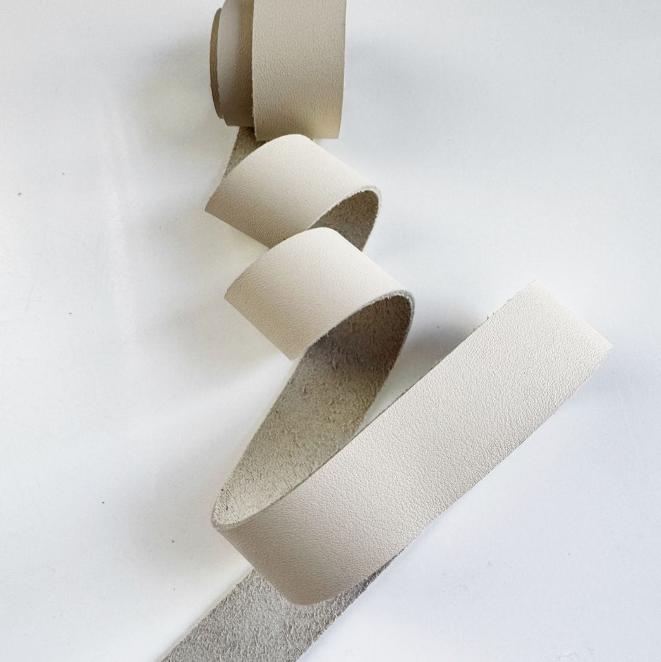 Coiled 1-inch wide cream-colored leather strap for purse and bag handles on a white background.