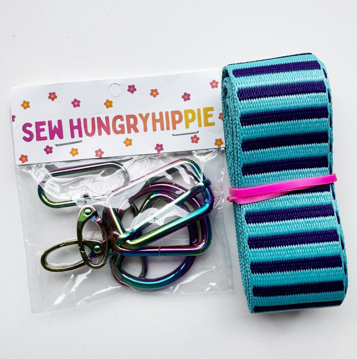 Sew Hungry Hippie rainbow hardware pack with rainbow metal clasps and a roll of striped webbing strap.