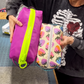 Purple pouch with an oversized neon green chunky zipper beside a cream strawberry-print pouch with a metallic coil zipper