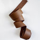 Coiled 1-inch wide medium brown leather strap for bag making on a white background.