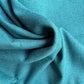 A close-up of draped teal blue fabric with a visible woven texture, filling the entire frame.