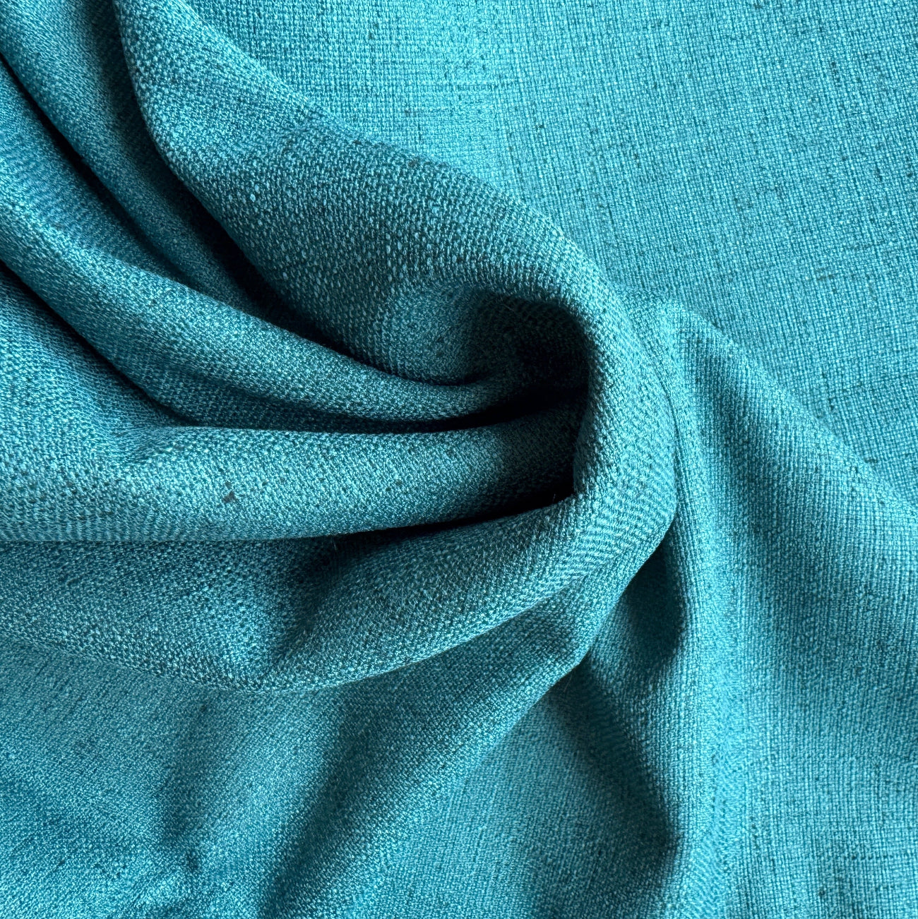 A close-up of draped teal blue fabric with a visible woven texture, filling the entire frame.