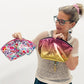 Woman holding a floral makeup bag and a pink metallic pouch against a white background