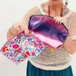 Person holding two clutch bags, one floral and one metallic pink, against a white background