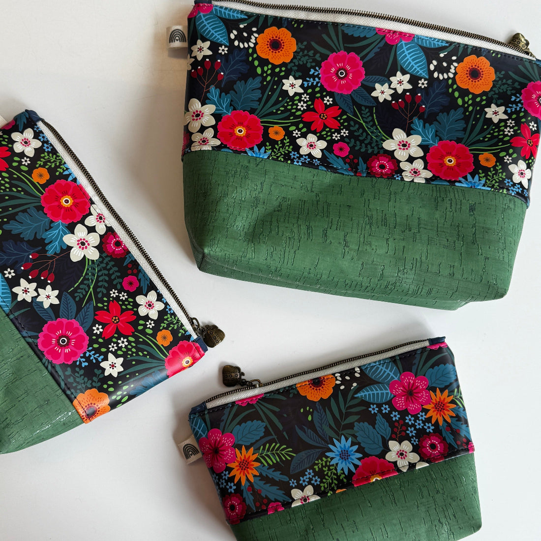Three floral-patterned pouches with green base on a white surface