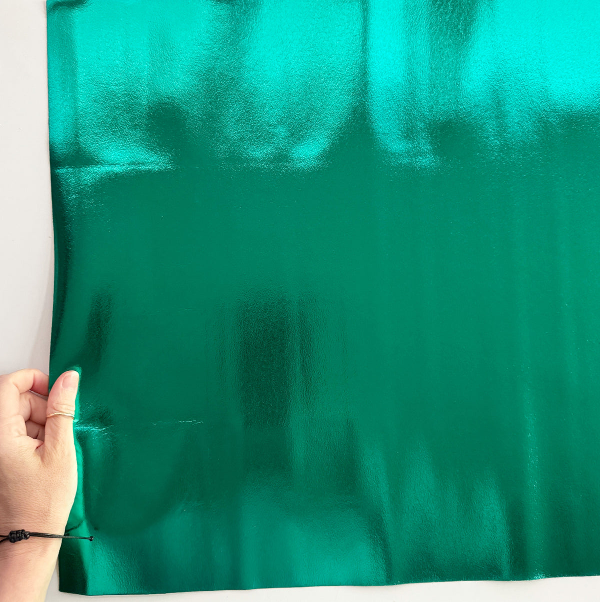 Close-up of shiny emerald green metallic foil fabric with a smooth, reflective finish against a white background.