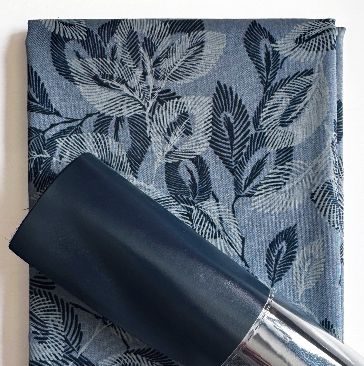Roll of black fabric with a blue fabric featuring leaf pattern in the background
