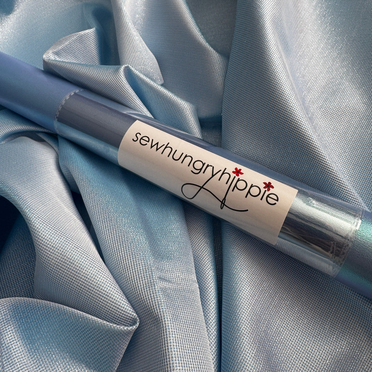 Sewing needle with a visible brand label on a light blue fabric background