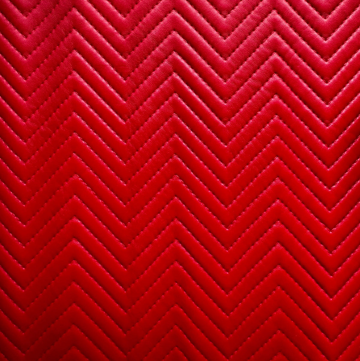 A close-up of a red chevron-patterned quilted fabric with stitched zigzag lines.