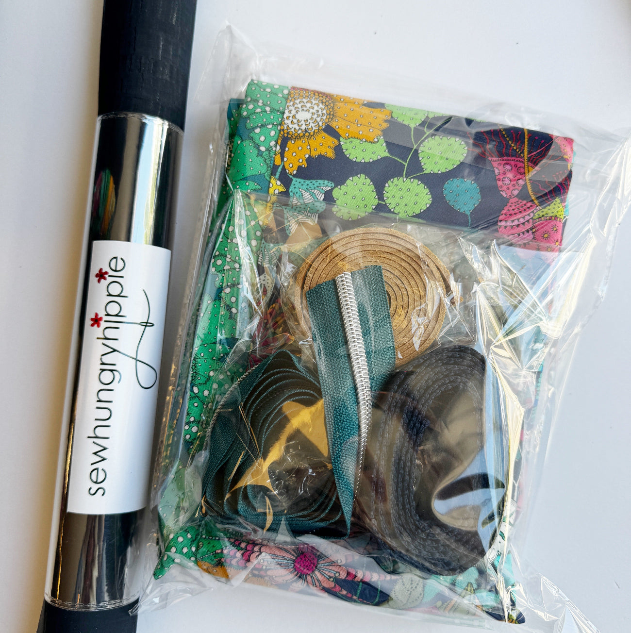 Packaged sewing kit with ribbons and a pen on a white background