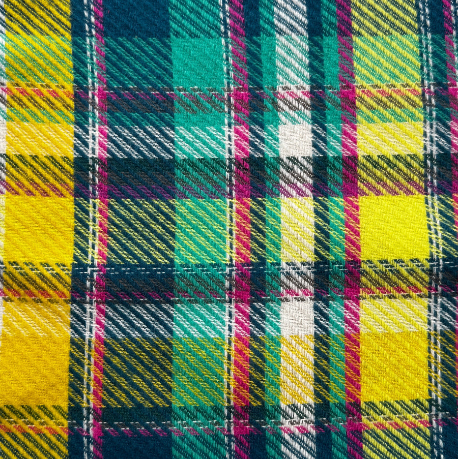 A close-up of a colorful tartan plaid fabric pattern with yellow, teal, navy, pink, and white stripes.