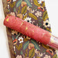 Muted brown floral fabric with green leaves and white flowers paired with a roll of coral pink cork fabric featuring gold foil accents.