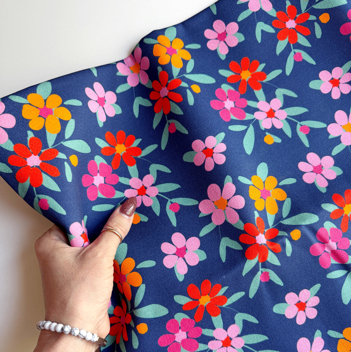 Hand holding fabric with colorful floral pattern on a blue background